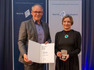 Bernadette Felsch – langjähriges Mitglied des Münchner Forums – erhält die Bezirksmedaille des Bezirks Oberbayern Bezirkstagspräsident Thomas Schwarzenberger überreicht die Auszeichnung an Bernadette Felsch